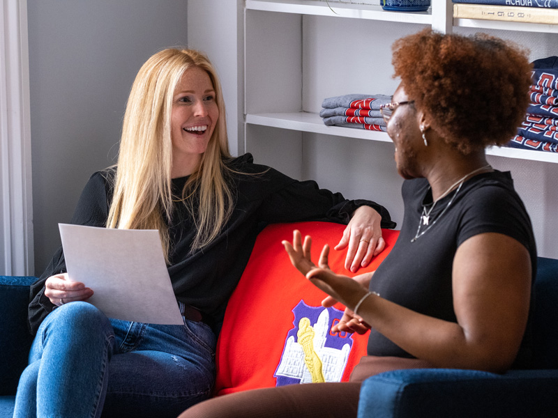 Campus Tour coordinator Leah Vasil smiles while speaking with a student in a reception room.